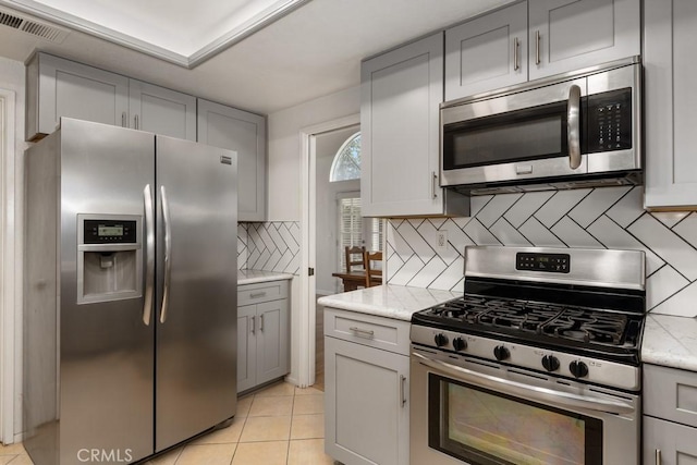 kitchen with stainless steel appliances, light stone countertops, light tile patterned floors, and backsplash