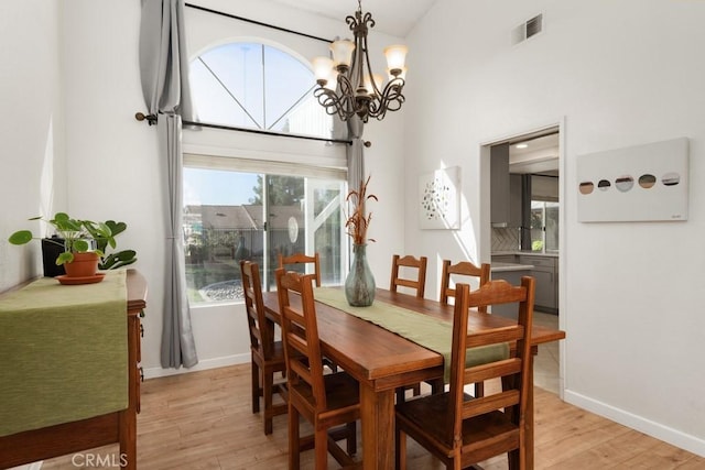 dining space featuring an inviting chandelier, light hardwood / wood-style floors, and a high ceiling