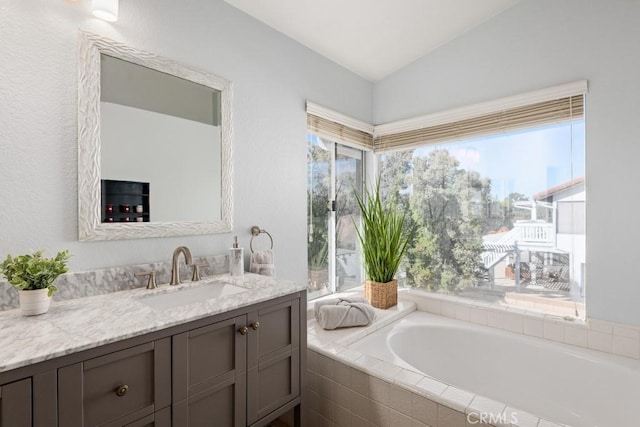 bathroom with vanity, tiled tub, and vaulted ceiling