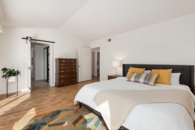 bedroom featuring lofted ceiling, wood-type flooring, and a barn door