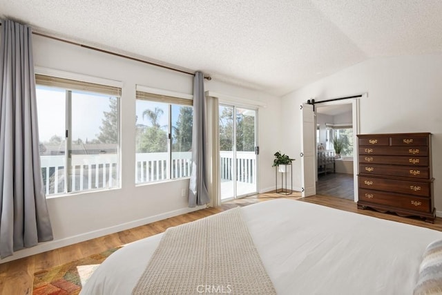 bedroom featuring lofted ceiling, wood-type flooring, a textured ceiling, access to outside, and a barn door