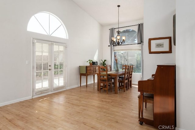 dining area featuring an inviting chandelier, a towering ceiling, light hardwood / wood-style flooring, and french doors