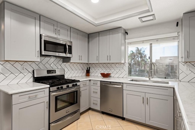 kitchen with stainless steel appliances, a tray ceiling, sink, and gray cabinetry