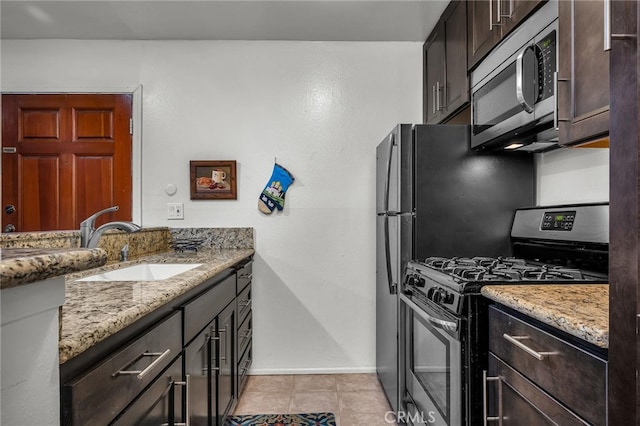 kitchen with appliances with stainless steel finishes, sink, light tile patterned floors, dark brown cabinetry, and light stone countertops