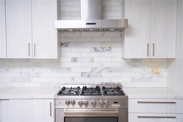 kitchen featuring tasteful backsplash, light stone countertops, wall chimney range hood, white cabinetry, and gas stove