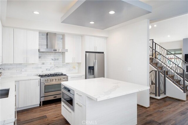 kitchen with a kitchen island, white cabinetry, stainless steel appliances, dark wood-type flooring, and wall chimney range hood