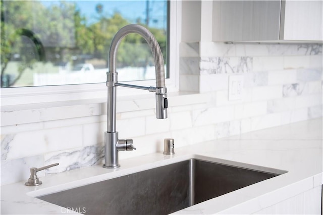 interior details with backsplash, a sink, and light stone countertops