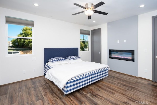 bedroom featuring dark wood-style floors, recessed lighting, a glass covered fireplace, and a ceiling fan