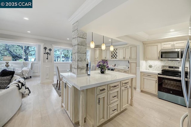 kitchen featuring pendant lighting, a kitchen island with sink, stainless steel appliances, crown molding, and cream cabinets