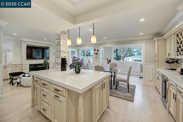 kitchen with a fireplace, hanging light fixtures, light hardwood / wood-style floors, crown molding, and cream cabinets