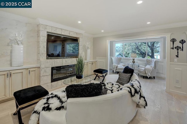 living room with a tiled fireplace, crown molding, and light hardwood / wood-style floors