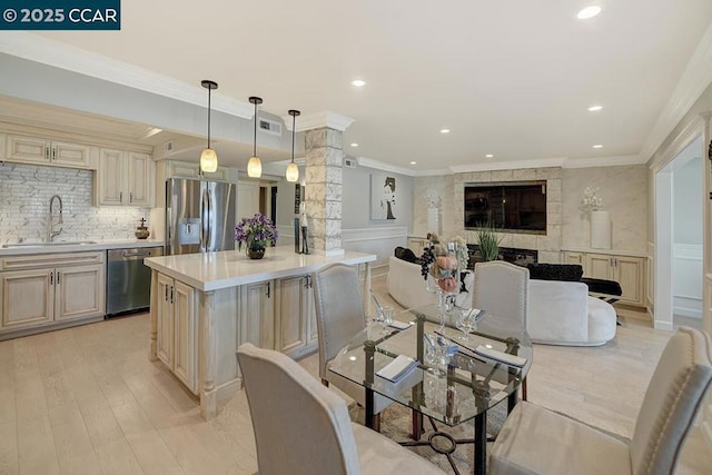 dining room featuring decorative columns, crown molding, sink, and light wood-type flooring