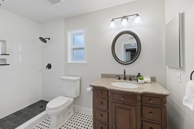 bathroom with tiled shower, vanity, and toilet