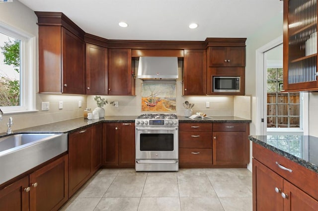 kitchen with appliances with stainless steel finishes, sink, backsplash, dark stone counters, and wall chimney exhaust hood