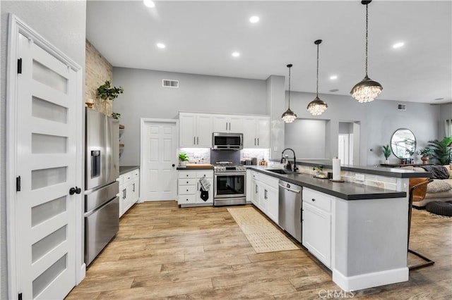 kitchen with visible vents, a peninsula, a sink, stainless steel appliances, and dark countertops