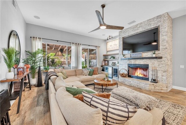 living room featuring ceiling fan, a stone fireplace, and light wood-type flooring