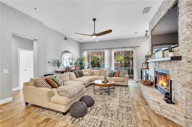 living room featuring ceiling fan, a fireplace, and light wood-type flooring