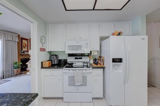 kitchen with white cabinetry, light tile patterned floors, dark stone countertops, white appliances, and a fireplace