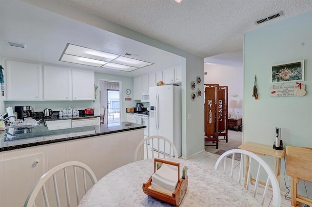 kitchen featuring a textured ceiling, light tile patterned floors, white appliances, dark stone counters, and white cabinets