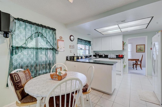 kitchen with white cabinets, white fridge, light tile patterned floors, kitchen peninsula, and a textured ceiling