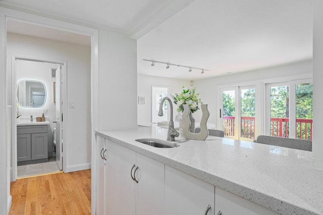 kitchen featuring sink, white cabinetry, light hardwood / wood-style flooring, track lighting, and light stone countertops