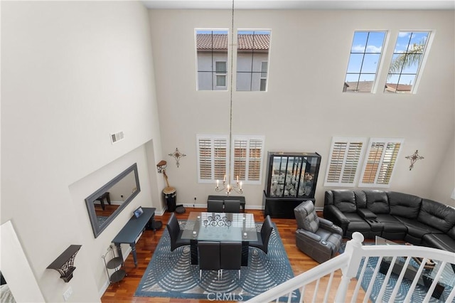 living room featuring an inviting chandelier, plenty of natural light, wood-type flooring, and a high ceiling