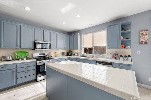 kitchen featuring stainless steel appliances, sink, tile counters, and blue cabinetry