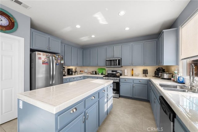 kitchen with sink, blue cabinetry, a kitchen island, stainless steel appliances, and light tile patterned flooring