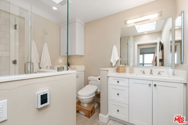 bathroom featuring a skylight, toilet, vanity, and a shower with shower door