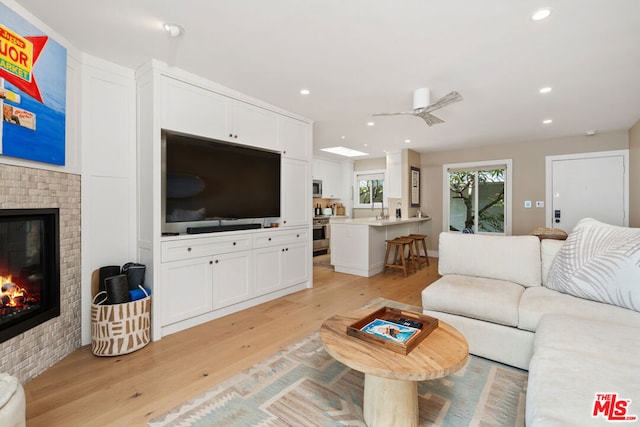 living room featuring ceiling fan, a fireplace, and light hardwood / wood-style floors