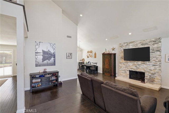 living room featuring dark hardwood / wood-style flooring, a stone fireplace, and high vaulted ceiling