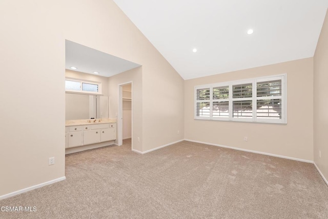 unfurnished bedroom featuring multiple windows, high vaulted ceiling, a walk in closet, and light colored carpet