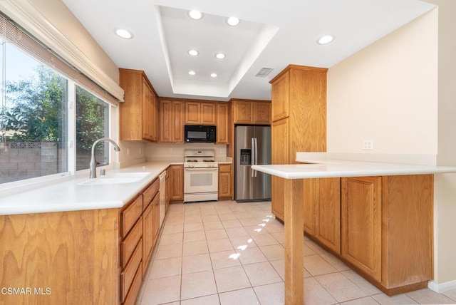 kitchen with kitchen peninsula, sink, light tile patterned floors, a tray ceiling, and white appliances