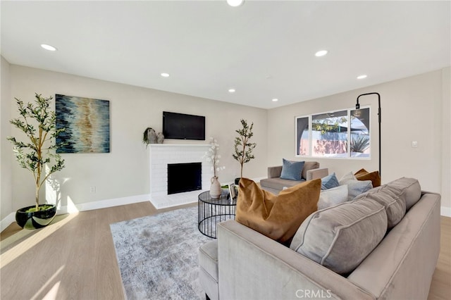 living room featuring baseboards, recessed lighting, a brick fireplace, and light wood-style floors