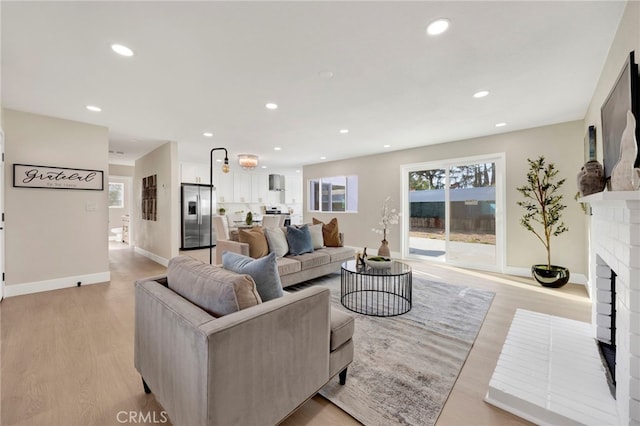 living area featuring baseboards, a fireplace, light wood-style flooring, and recessed lighting