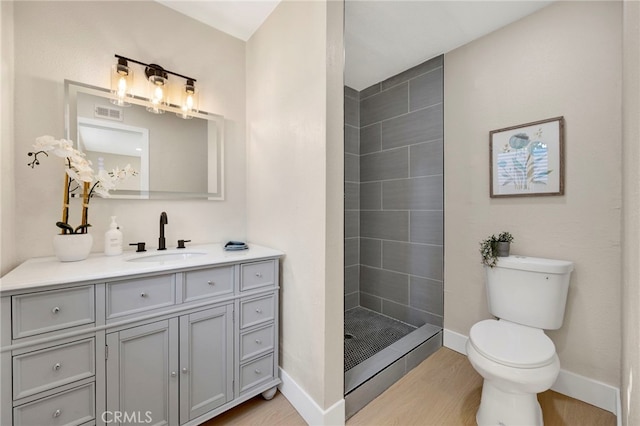 full bathroom featuring toilet, wood finished floors, vanity, baseboards, and tiled shower