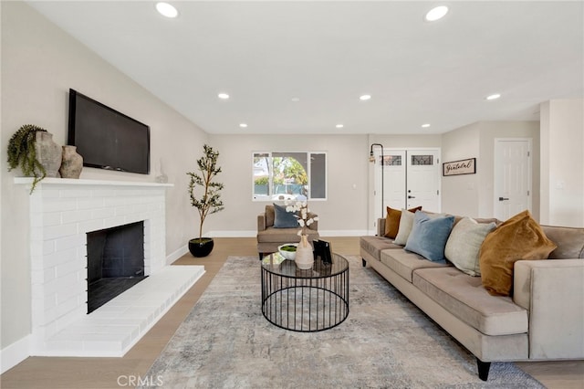 living room with recessed lighting, a brick fireplace, and wood finished floors