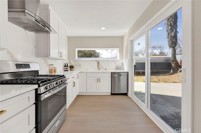 kitchen featuring light stone counters, stainless steel appliances, white cabinetry, backsplash, and wall chimney exhaust hood