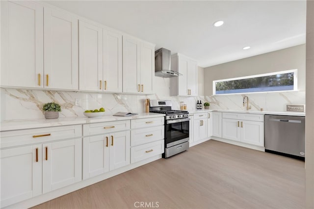 kitchen with a sink, white cabinets, appliances with stainless steel finishes, wall chimney range hood, and decorative backsplash