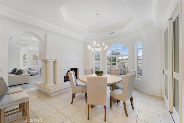 dining area featuring a fireplace, ornamental molding, light tile patterned floors, a notable chandelier, and a raised ceiling