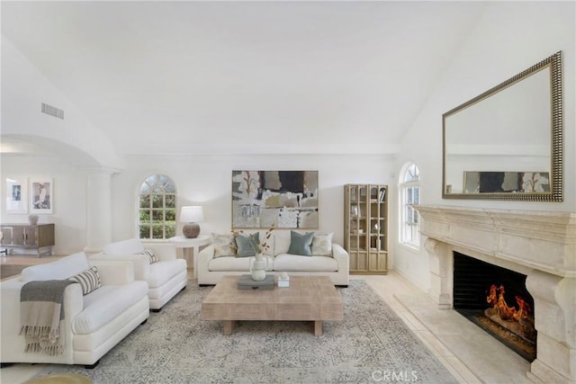 living room with a fireplace, a wealth of natural light, high vaulted ceiling, and decorative columns