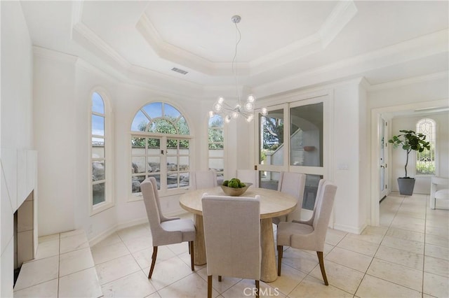 dining space with a notable chandelier, a tray ceiling, ornamental molding, light tile patterned flooring, and french doors