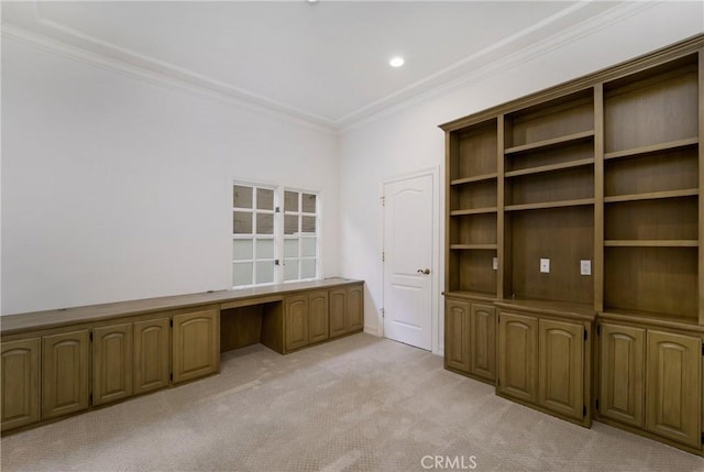 unfurnished office featuring crown molding, built in desk, and light colored carpet