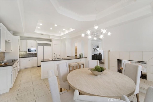 dining room with light tile patterned floors, sink, crown molding, a tiled fireplace, and a raised ceiling