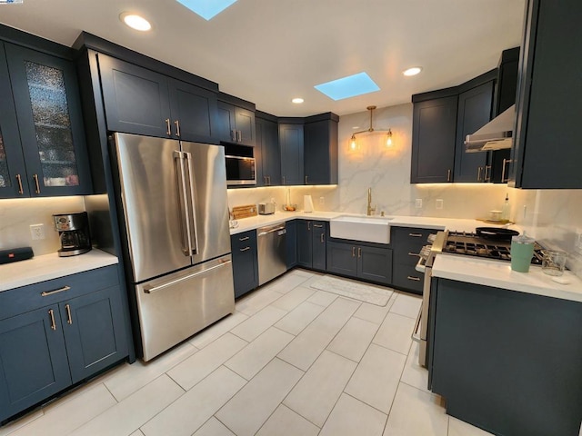 kitchen featuring a skylight, sink, decorative backsplash, hanging light fixtures, and stainless steel appliances