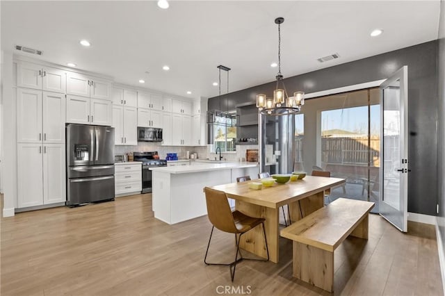 kitchen with decorative light fixtures, white cabinetry, sink, stainless steel appliances, and light hardwood / wood-style flooring