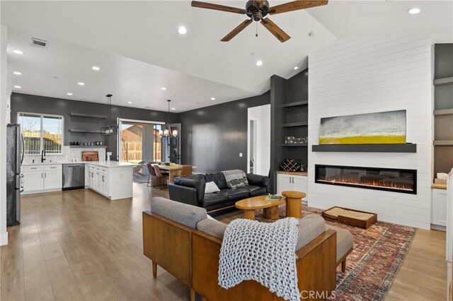 living room featuring sink, built in features, ceiling fan, vaulted ceiling, and light wood-type flooring