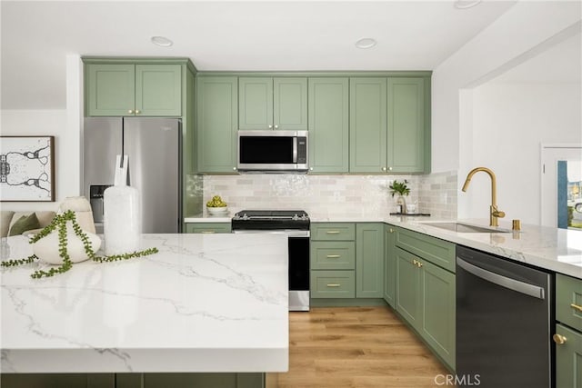 kitchen with green cabinets, stainless steel appliances, light stone countertops, and sink