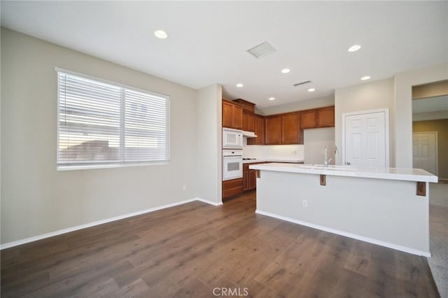 kitchen with sink, white appliances, a kitchen island with sink, a kitchen breakfast bar, and dark hardwood / wood-style flooring