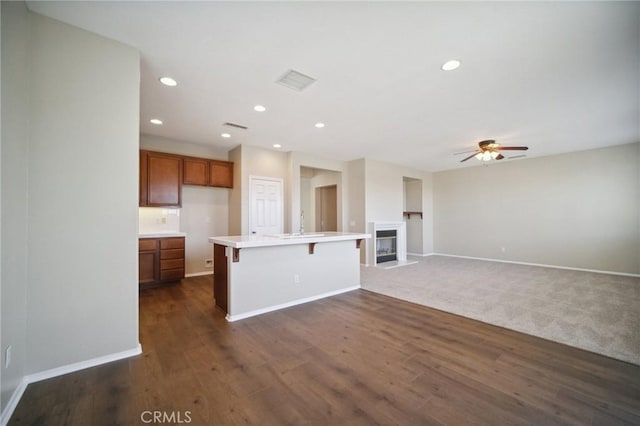 kitchen with a center island with sink, ceiling fan, a breakfast bar area, and dark hardwood / wood-style flooring